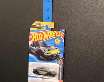 May include: A Hot Wheels toy car packaging featuring a black and green car with yellow accents. The packaging also includes a red car and the text "Hot Wheels Legends Tour Winner!" and "New for 2025".