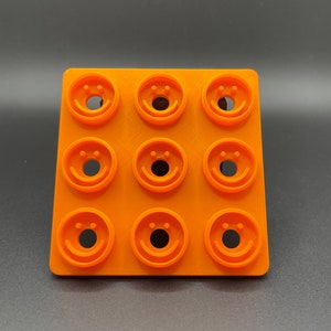 May include: Orange plastic mold with nine circular depressions, each featuring a smiley face design.