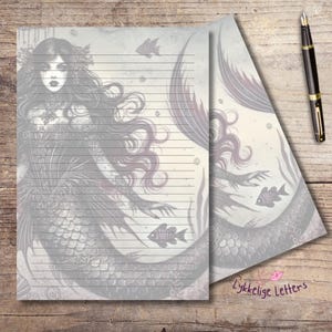Puede incluir: Dos hojas de papel de carta rayado con una ilustración en escala de grises de una sirena con cabello largo y fluido, escamas y flora submarina. Una pluma estilográfica negra con detalles dorados descansa a la derecha del papel, que muestra el texto Lykkelige Letters.