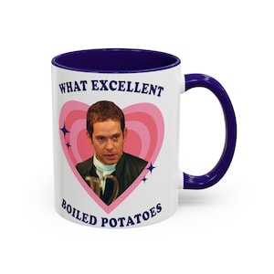 Puede incluir: Taza de cerámica blanca con interior y asa azul marino. La taza presenta un diseño de corazón rosa con un retrato de hombre y el texto "WHAT EXCELLENT BOILED POTATOES" en azul marino. También se incluyen cuatro estrellas azules.