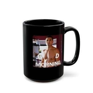 May include: A black ceramic mug featuring a printed image of a shirtless man with short dark hair. The text "GOOD MORNING" is printed in white capital letters over the image, with "GOOD" positioned near the top and "MORNING" at the bottom.