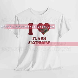 Puede incluir: Camiseta blanca con una "I" roja y un corazón que contiene la imagen de una persona. Debajo del corazón, el texto dice "FLASH SLOTHMORE". La camiseta tiene cuello redondo.