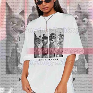 May include: White unisex t-shirt featuring a black and white graphic of characters from the animated film, Zootopia. The shirt includes the text "NICK WILDE" at the bottom. The model is wearing a 2XL shirt.