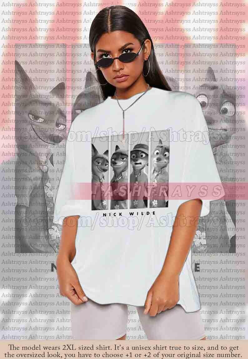 May include: White unisex t-shirt featuring a black and white graphic of characters from the animated film, Zootopia. The shirt includes the text "NICK WILDE" at the bottom. The model is wearing a 2XL shirt.
