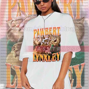 May include: White unisex t-shirt featuring the text "PAWBERT LYNXLEY" in orange and yellow, with a cartoon image of three lynx. The shirt is oversized and made of a soft material.