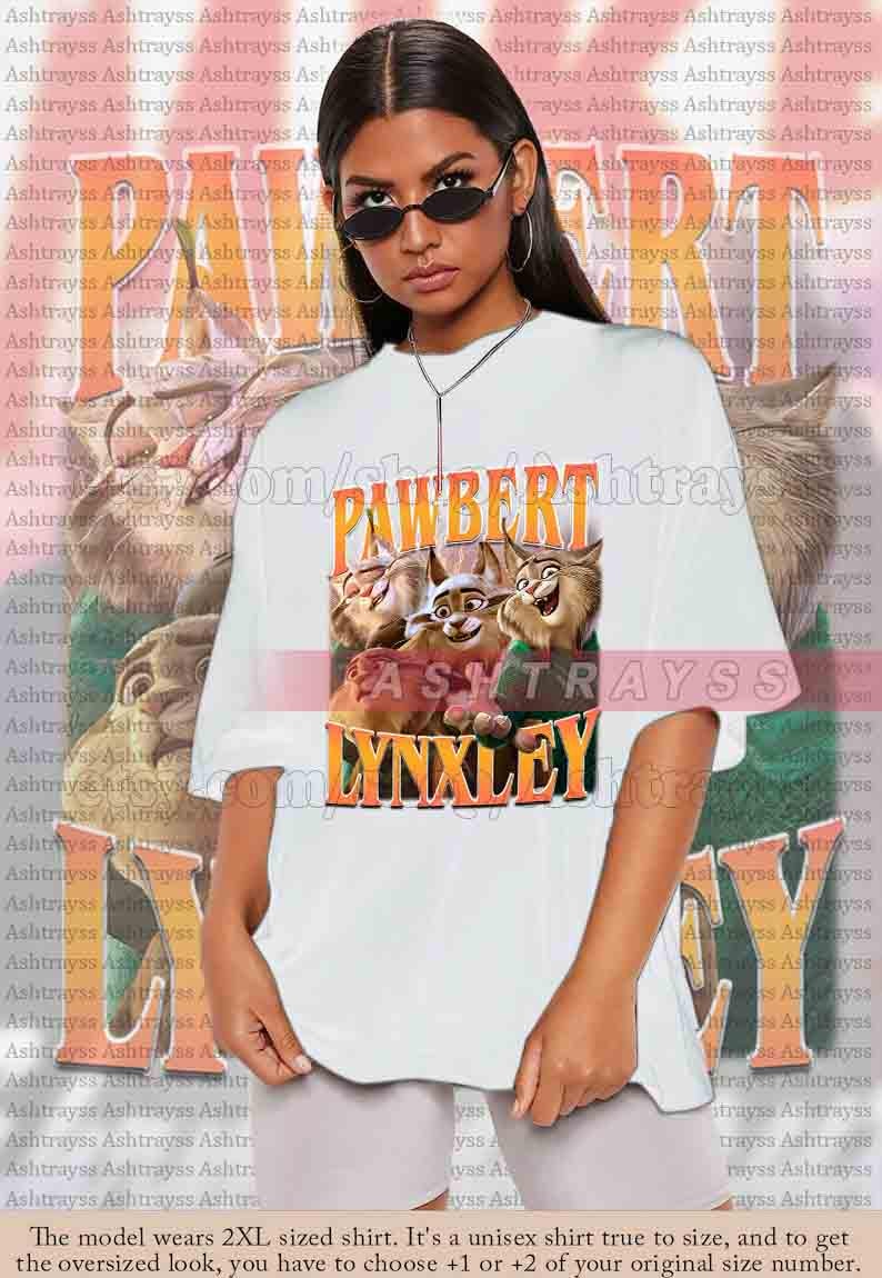 May include: White unisex t-shirt featuring the text "PAWBERT LYNXLEY" in orange and yellow, with a cartoon image of three lynx. The shirt is oversized and made of a soft material.