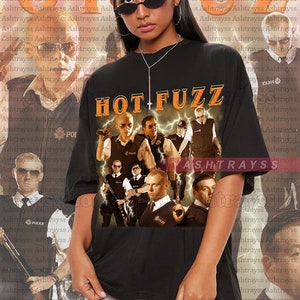 May include: Black unisex t-shirt with the film title "HOT FUZZ" in orange and yellow. The shirt features a collage of images from the film, including actors in police uniforms. The model is wearing black sunglasses.