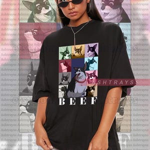 Puede incluir: Camiseta unisex negra con una cuadrícula de ilustraciones de perros de dibujos animados y la palabra "BEEF". La persona que lleva la camiseta lleva gafas de sol. La modelo lleva una talla 2XL.