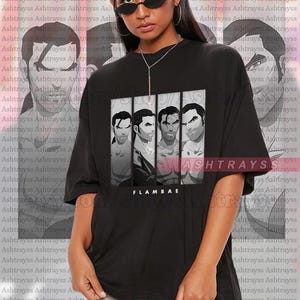 May include: Black unisex t-shirt featuring a graphic of four stylized male figures in a vertical panel. The word "FLAMBAE" is printed below the graphic. The model is wearing a 2XL shirt.