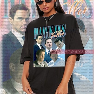 May include: Black oversized t-shirt featuring a graphic of actors with the text "HAWKINS Fuller" in a vintage style. The shirt is a unisex style and is available in 2XL size.