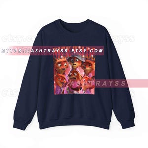 Puede incluir: Sudadera azul marino con un estampado gr&aacute;fico de zorros de dibujos animados y el texto "NICK WILDE". El dise&ntilde;o presenta varios zorros en diferentes poses, sobre un fondo rosa, en un estilo retro.