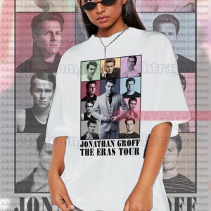 May include: White unisex t-shirt featuring a collage of images of Jonathan Groff. The shirt includes the text "JONATHAN GROFF THE ERAS TOUR" in a bold, black font. The model is wearing a 2XL shirt.