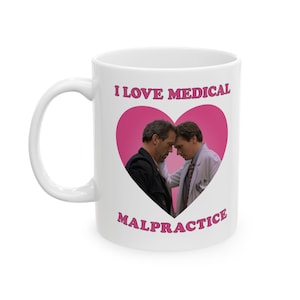 Puede incluir: Taza de café de cerámica blanca con un diseño de corazón rosa con dos hombres. El texto "Me encanta la mala praxis médica" está impreso en la taza.