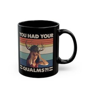 Puede incluir: Una taza de cerámica negra con un estampado gráfico de una persona con astas de ciervo en la cabeza. El diseño incluye un fondo de atardecer retro con rayas horizontales en naranja, amarillo y azul, y el texto YOU HAD YOUR QUALMS?!