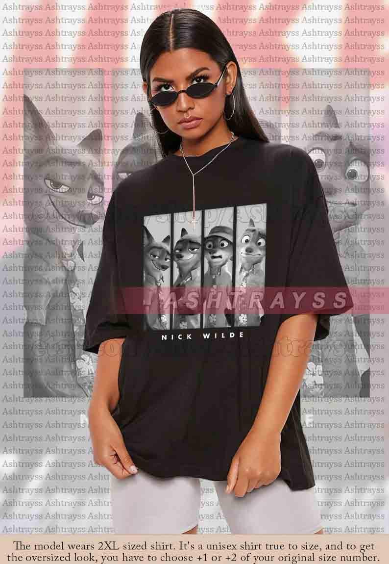 May include: Black unisex t-shirt featuring a graphic of characters from the animated film "Zootopia." The design includes Nick Wilde's name. The model is wearing a 2XL shirt.