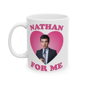 Pode incluir: Caneca de cerâmica branca com o texto "NATHAN FOR ME" em letras rosa. A caneca apresenta um coração rosa com um homem de terno. A caneca tem uma alça branca.