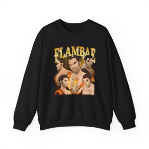 Puede incluir: Sudadera negra de cuello redondo con un diseño gráfico retro. El diseño presenta a un hombre en varias poses y la palabra "FLAMBAE" en dorado. La sudadera está hecha de un material suave y es adecuada para uso casual.