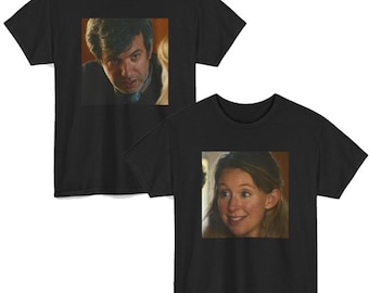 May include: Two black short-sleeved t-shirts featuring square photographic prints on the chest. The top shirt displays a man with dark hair looking forward, while the bottom shirt shows a woman with light brown hair smiling slightly.