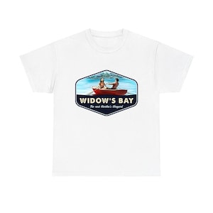 Puede incluir: Una camiseta blanca con un gráfico central de un bote de remos rojo sobre agua azul con dos personas remando. El diseño está encerrado en un hexágono azul oscuro con el texto WIDOW'S BAY y The next Martha's Vineyard impreso en blanco.