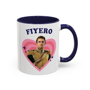 May include: White ceramic mug with a navy blue interior and handle. The mug features the word "FIYERO" in blue above a pink heart design. Inside the heart is a portrait of a man in a military-style uniform.