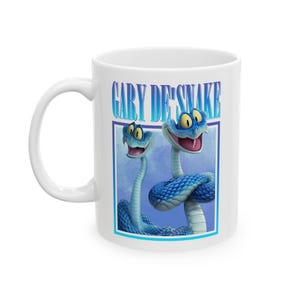 Puede incluir: Taza de cerámica blanca con una ilustración de dibujos animados de dos serpientes azules con ojos amarillos y bocas abiertas. La taza tiene el texto "GARY DE'SNAKE" en letras azules y blancas. Las serpientes están dentro de un marco rectangular azul.
