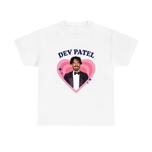 May include: White t-shirt with a graphic of Dev Patel in a tuxedo inside a pink heart. The text "DEV PATEL" is arched above the heart in blue. The design includes pink stars and a bow tie.