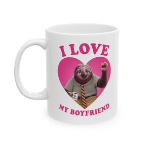 Puede incluir: Taza de cerámica blanca con un perezoso de dibujos animados dentro de un corazón rosa, con las palabras "I LOVE MY BOYFRIEND". El perezoso lleva camisa y corbata y sostiene una taza de café.