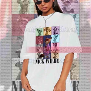 Peut inclure: T-shirt unisexe blanc avec une grille color&eacute;e de personnages de dessins anim&eacute;s et le texte "NICK WILDE". Le t-shirt a des manches courtes et une coupe d&eacute;contract&eacute;e, id&eacute;al pour un usage quotidien.