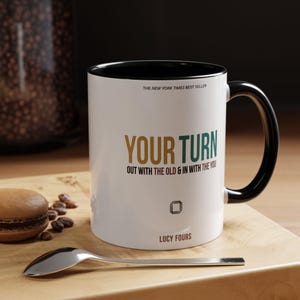 Puede incluir: Una taza de cerámica blanca con interior y asa negros. El texto dice THE NEW YORK TIMES BEST SELLER, YOUR TURN, OUT WITH THE OLD & IN WITH THE YOU y LUCY FOURS. Un pequeño icono cuadrado con cuatro formas de lápiz está centrado debajo.