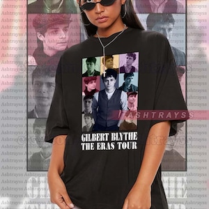 May include: Black t-shirt featuring a collage of photographs of a person. The text "GILBERT BLYTHE THE ERAS TOUR" is printed on the shirt.