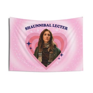 May include: Pink wall hanging with the text "SHAUNNIBAL LECTER" in navy blue. The image features a woman inside a pink heart design, surrounded by blue star accents and a sparkling background.