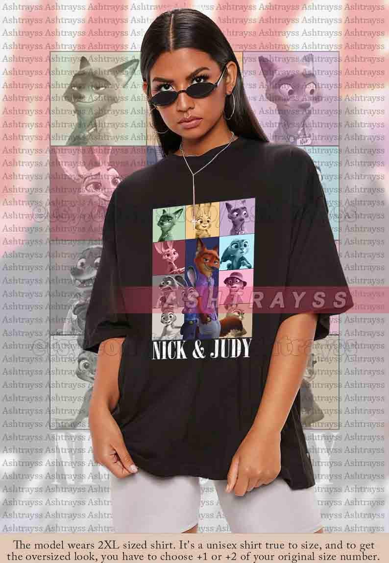 May include: Black unisex t-shirt featuring a colorful graphic of characters from the animated film "Zootopia." The design includes Nick Wilde and Judy Hopps, with the text "NICK & JUDY" below. The shirt is oversized.
