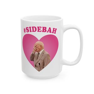 May include: A white ceramic mug featuring a large pink heart graphic on the front. Inside the heart is a photograph of a person in a tan suit covering their face with their hand. Above the heart, the text #SIDEBAH is printed in pink letters.