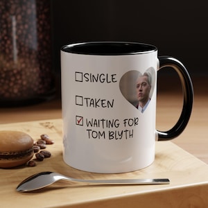 May include: A white ceramic mug with a black interior and handle. The front features a checklist with the text Single, Taken, and a ticked box next to Waiting for Tom Blyth, accompanied by a heart-shaped photograph of the actor Tom Blyth.