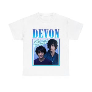 Pode incluir: Uma t-shirt branca com uma impressão gráfica com o texto DEVON em letras com gradiente azul acima de uma moldura quadrada contendo duas imagens de uma pessoa de cabelo escuro, com o nome Bostick escrito em letra branca sobre o fundo azul.
