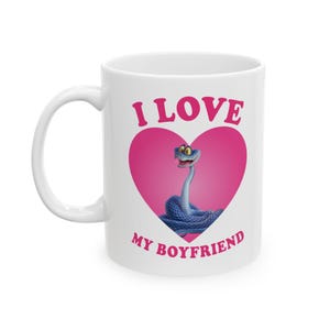 May include: White ceramic mug with a pink heart and a cartoon snake illustration. The text "I LOVE MY BOYFRIEND" is printed on the mug in pink. The mug has a white handle and a white interior.