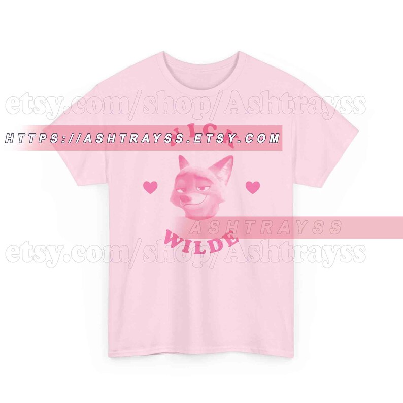 May include: A light pink t-shirt featuring a cartoon fox face with the text "Wilde" below it. Two pink hearts flank the fox image. The text "https://ashtrayss.etsy.com" is printed across the top of the shirt.