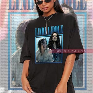 Könnte beinhalten: Schwarzes Unisex-T-Shirt mit dem Text "LINDA LIDDLE" in Blau und einer Filmplakat-Grafik. Die Grafik zeigt zwei Personen. Das Model trägt eine Sonnenbrille und eine Halskette.