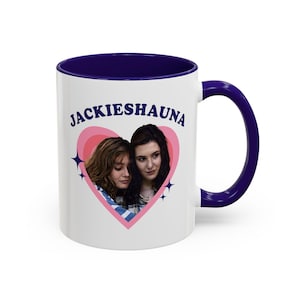 May include: White ceramic mug with a navy blue interior and handle. The mug features a pink heart design with two women's faces and the text "JACKIESHAUNA" in blue. Two blue starbursts flank the heart.