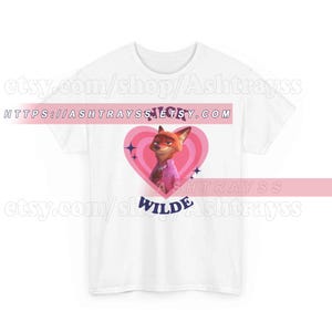May include: White t-shirt featuring a cartoon fox character inside a pink heart. The fox is wearing a pink shirt and tie. The text "NICK WILDE" is below the heart. The Etsy shop URL is visible.