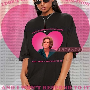 Può includere: T-shirt unisex nero con un cuore rosa, un ritratto e la scritta "I DON'T UNDERSTAND THE QUESTION AND I WON'T RESPOND TO IT." La maglietta oversize è realizzata in tessuto morbido.