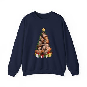 May include: Navy blue sweatshirt featuring a Christmas tree design made of illustrated faces. The tree is adorned with a gold star and surrounded by wrapped gifts. A festive and unique holiday-themed apparel item.