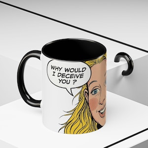 May include: A white ceramic mug with a black interior and handle, featuring a pop art illustration of a blonde person with blue eyes and a speech bubble containing the black text, "WHY WOULD I DECEIVE YOU ?" in a bold, comic book style font.