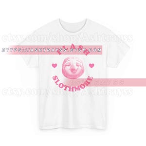 Puede incluir: Camiseta blanca con un diseño de perezoso rosa. El diseño incluye las palabras "Please Slothmore" y dos corazones rosas. La URL de la tienda Etsy es visible en la parte superior de la imagen.