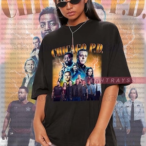 Puede incluir: Una camiseta negra con un estampado gráfico del reparto de la serie de televisión "Chicago P.D.". El gráfico presenta el título de la serie en letras doradas con rayos y una foto de grupo del reparto. La modelo lleva una camiseta talla 2XL.