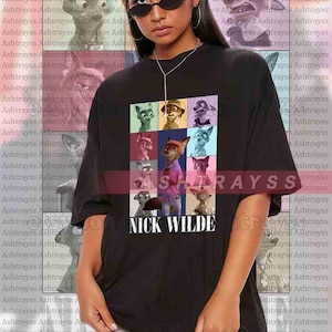 Peut inclure: T-shirt noir unisexe avec une grille color&eacute;e de personnages de dessins anim&eacute;s et le texte "NICK WILDE" en blanc. Le t-shirt a une coupe ample. Le mod&egrave;le porte du 2XL.