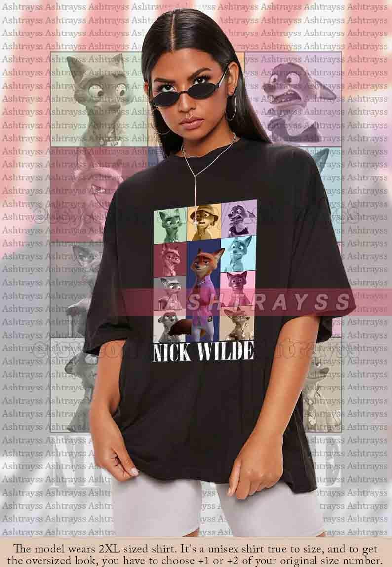 Peut inclure: T-shirt noir unisexe avec une grille color&eacute;e de personnages de dessins anim&eacute;s et le texte "NICK WILDE" en blanc. Le t-shirt a une coupe ample. Le mod&egrave;le porte du 2XL.