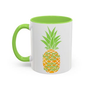 May include: White ceramic mug with a green rim and handle. The mug features a pineapple graphic with the text "did you hear about Pluto? that's messed up, right?"