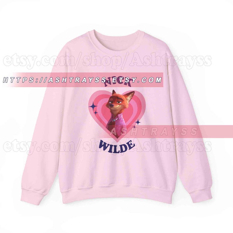 May include: A light pink sweatshirt featuring a cartoon image of Nick Wilde from Zootopia inside a pink heart. The sweatshirt has long sleeves and the name "Nick Wilde" is printed on the front.