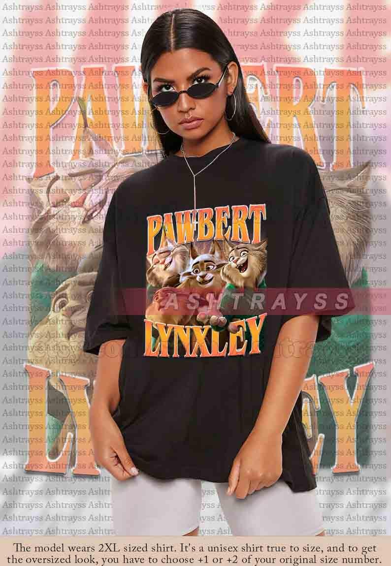 May include: Black unisex t-shirt featuring the text "PAWBERT LYNXLEY" in orange and yellow, with a cartoon image of three lynx-like characters. The shirt is oversized and made of a soft material.